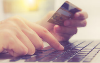 A hand holds a credit card, while the other hand types the numbers into an e-commerce site