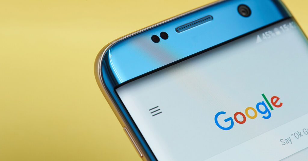 A blue smart phone showing the Google search home page, with a bright yellow background behind it