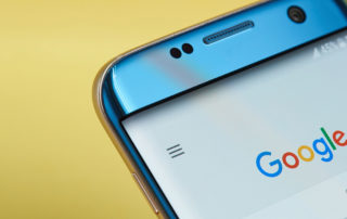 A blue smart phone showing the Google search home page, with a bright yellow background behind it