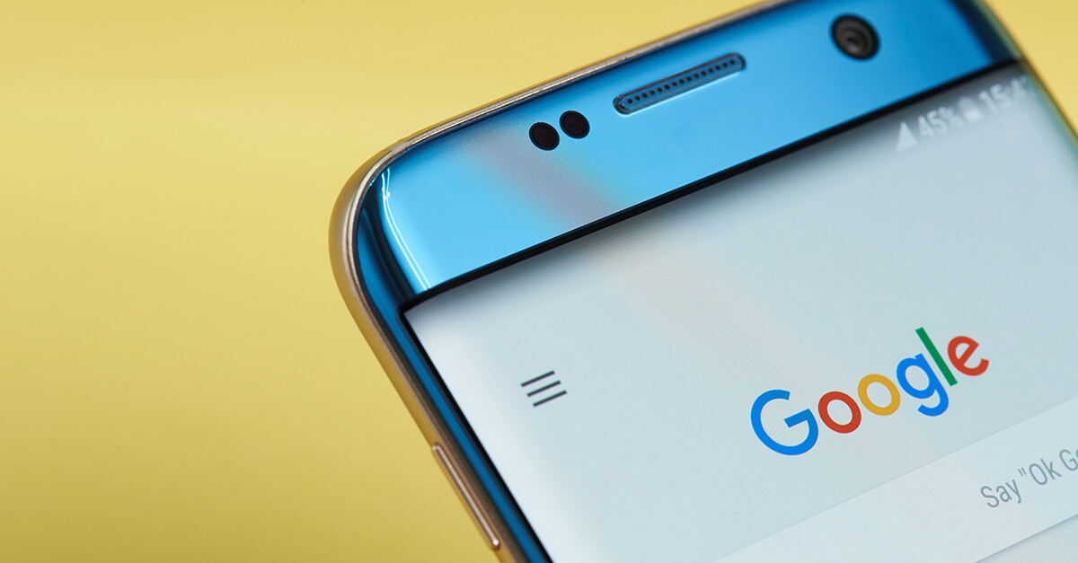 A blue smart phone showing the Google search home page, with a bright yellow background behind it