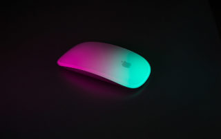 A computer mouse on black, highlighted by pink and teal light.