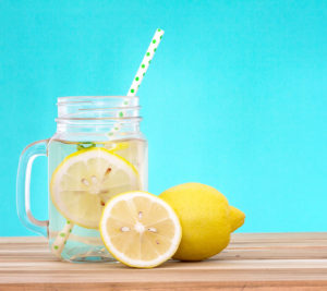 Lemonade served in a mason jar on a bright blue background, with sliced lemons surrounding it.
